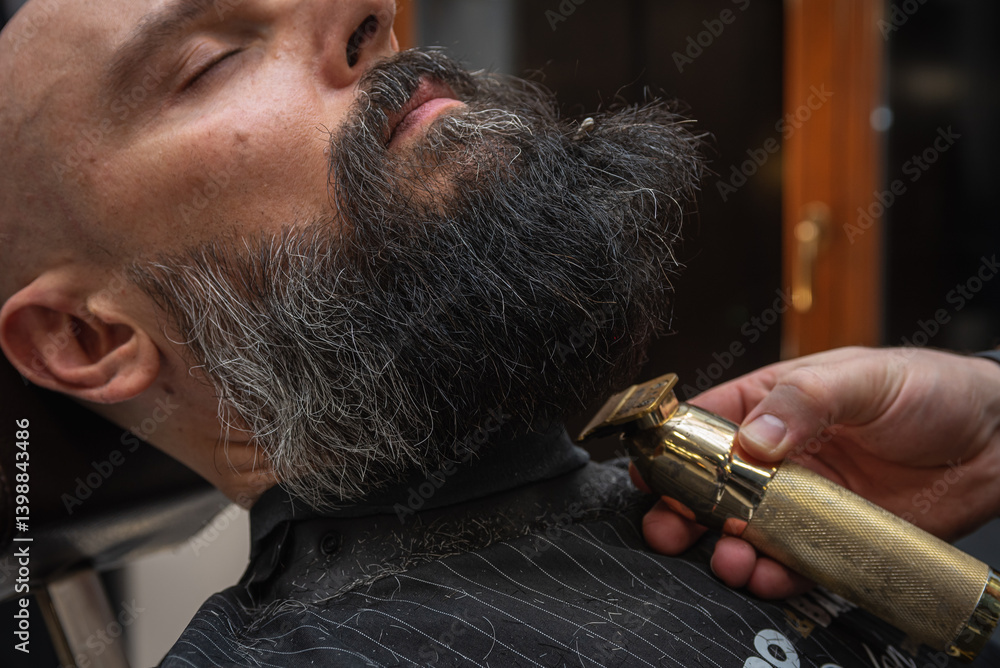 Close-up of a barber trimming a beard with electric clippers in a modern barbershop. Professional men's grooming and beard care service, selective focus