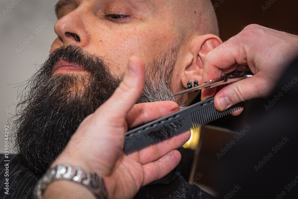 Close-up of a barber trimming a beard with electric clippers in a modern barbershop. Professional men's grooming and beard care service, selective focus