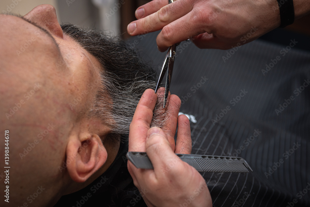 Close-up of a barber trimming a beard with electric clippers in a modern barbershop. Professional men's grooming and beard care service, selective focus
