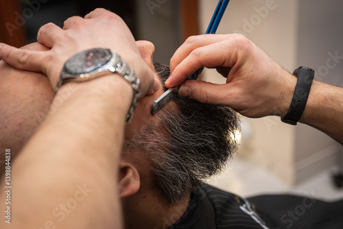 Obraz na płótnie Close-up of a barber trimming a beard with electric clippers in a modern barbershop. Professional men's grooming and beard care service, selective focus w salonie