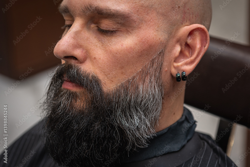 Close-up of a barber trimming a beard with electric clippers in a modern barbershop. Professional men's grooming and beard care service, selective focus