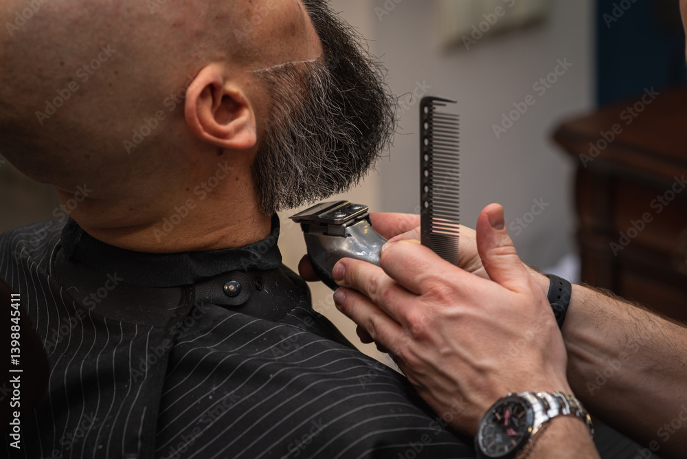 Close-up of a barber trimming a beard with electric clippers in a modern barbershop. Professional men's grooming and beard care service, selective focus