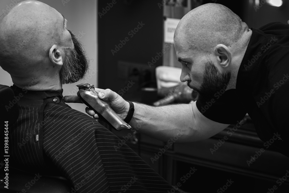 Black and white photo, close-up of a barber trimming a beard with electric clippers in a modern barbershop. Professional men's grooming and beard care, selective focus