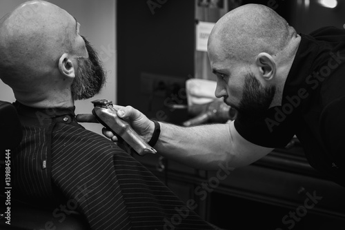 Obraz na płótnie Black and white photo, close-up of a barber trimming a beard with electric clippers in a modern barbershop. Professional men's grooming and beard care, selective focus w salonie