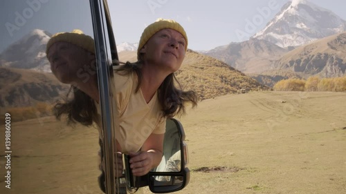 Woman traveler leans out of window of motorhome looking out over captivating mountain landscape