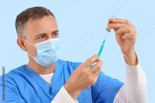 Mature doctor in medical mask with ampule and syringe on blue background