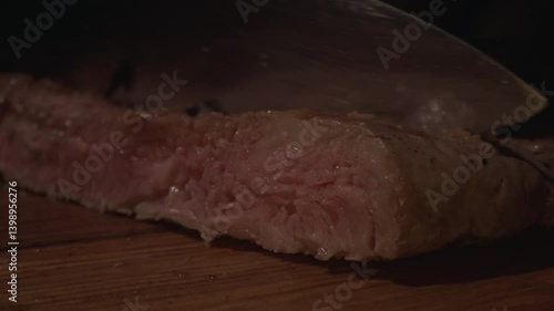 Male Chef hands cutting cooked beef steak with knife on wood cutting board, close up. Slow motion. Concepts food preparing process and restaurant service. 