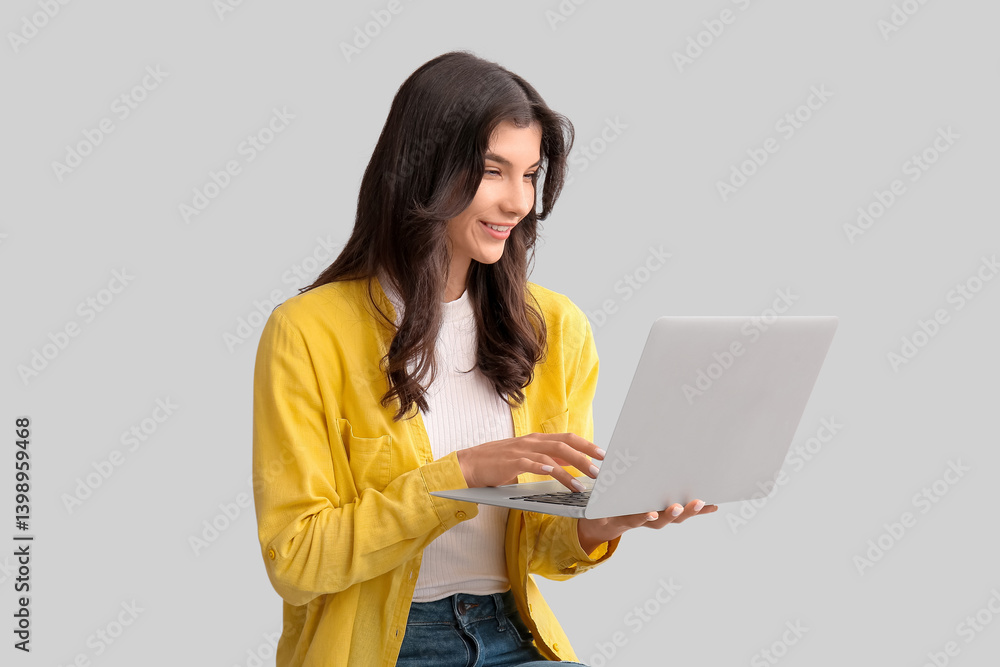 Fototapeta premium Beautiful young happy woman with laptop on grey background