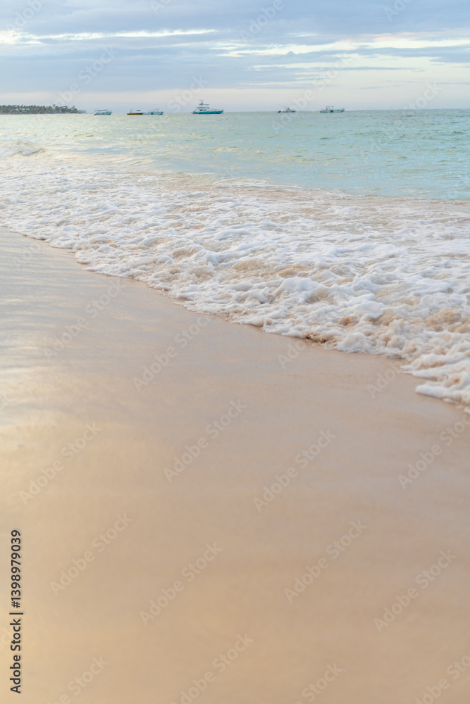 Waves gently lap against the serene sandy shore at sunset near the fishing boats in the distance Waves gently lap against the serene sandy shore at sunset near the fishing boats in the distance