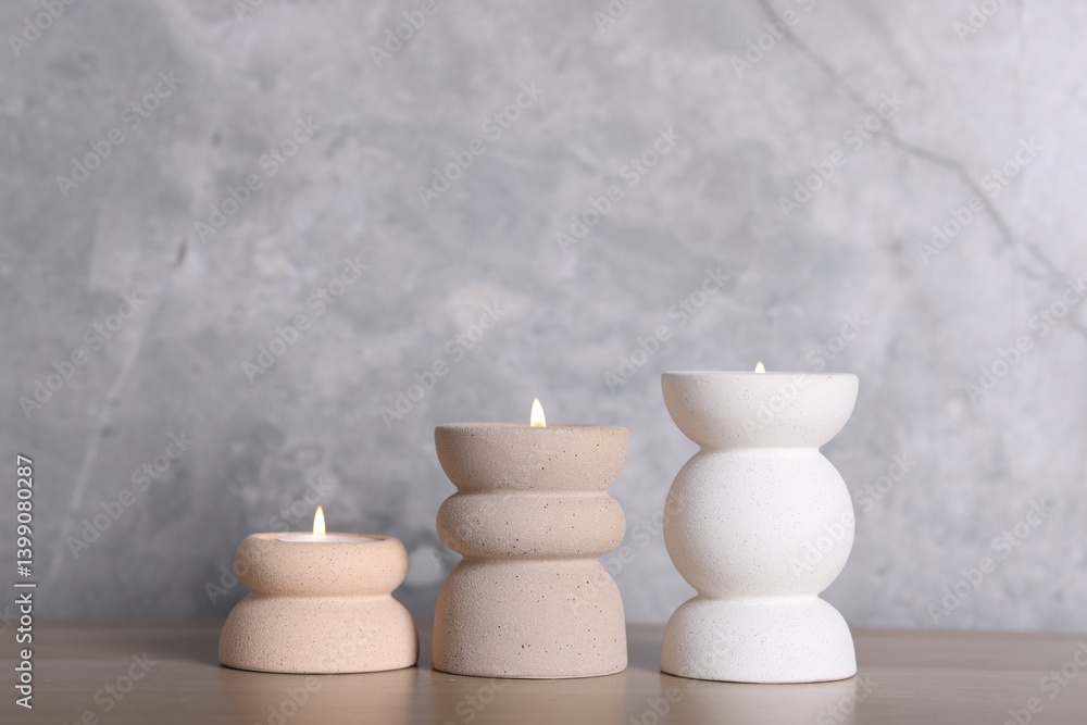 Stylish candlesticks with burning candles on wooden table near grey marble wall indoors Stylish candlesticks with burning candles on wooden table near grey marble wall indoors