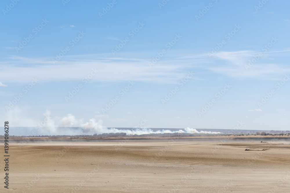 Smoke on the horizon from a wildfire near a dried lake bed during a drought on a windy day that is blowing dirt and dust Smoke on the horizon from a wildfire near a dried lake bed during a drought on a windy day that is blowing dirt and dust