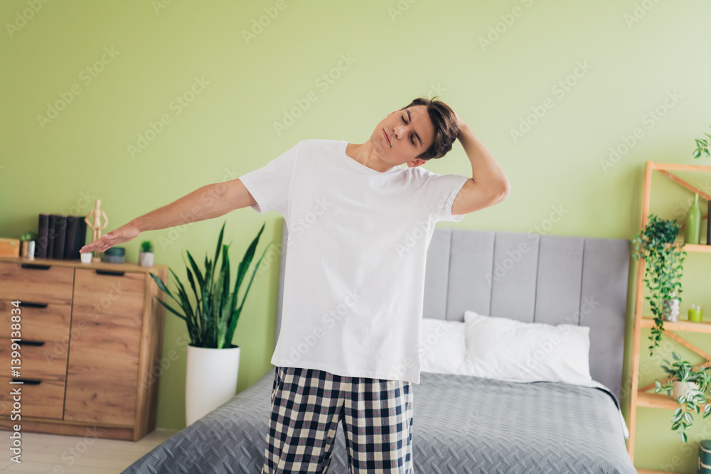 Young man stretching in bedroom morning indoors, feeling refreshed wearing plaid pajama pants, relaxing in comfortable sleepwear Young man stretching in bedroom morning indoors, feeling refreshed wearing plaid pajama pants, relaxing in comfortable sleepwear