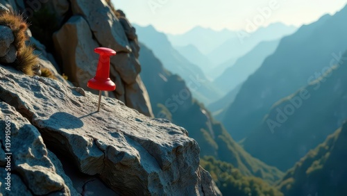 A vibrant red pushpin marks a significant location atop a rugged, grey rock formation overlooking a vast, serene mountain range bathed in soft sunlight.