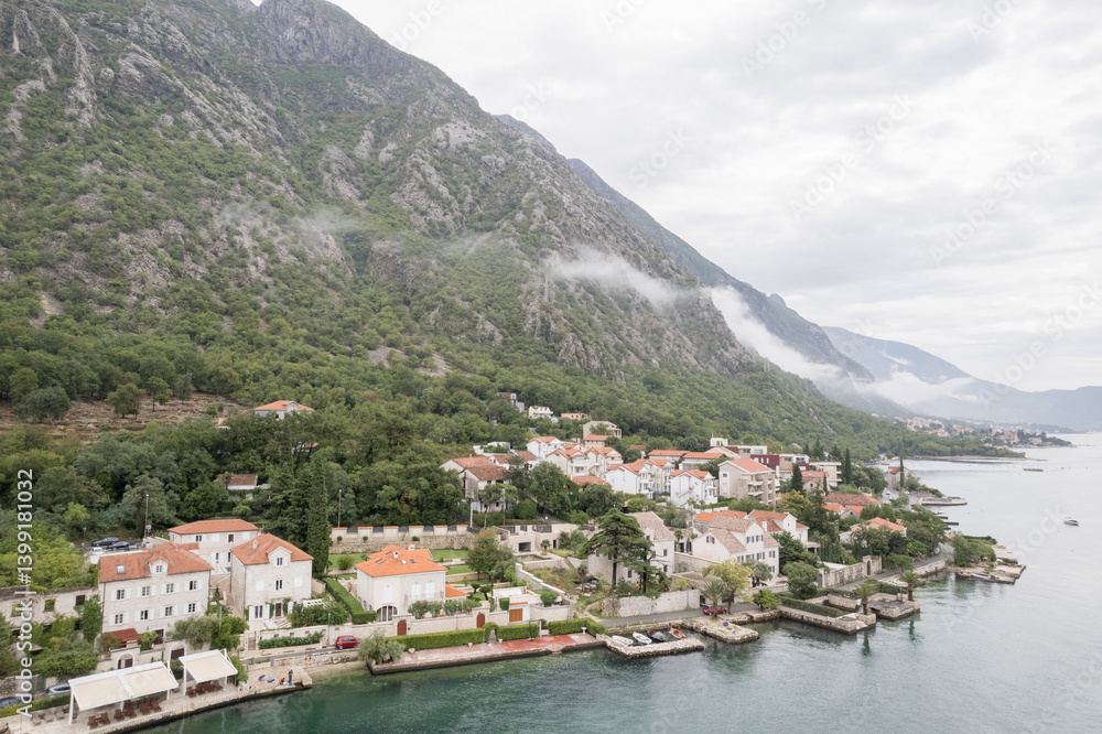 Fototapeta premium Ancient houses with red roofs at the foot of the mountains on the shores of the Bay of Kotor. Dobrota, Montenegro. Drone