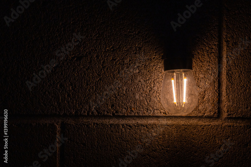 Filament In Lightbulb Glows Against Concrete Block Wall