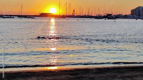 The sunset on Ibiza lights up the Mediterranean Sea creating contrasts A swimmer is seen in the water in video