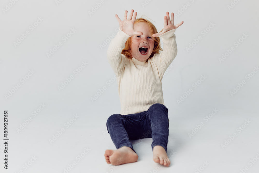 Happy little girl with hands in the air and a smile sitting on the floor, joy in childhood