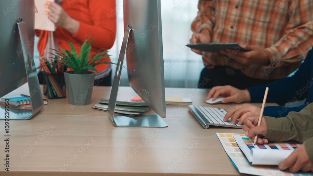 A dynamic office scene showing diverse professionals collaborating on design projects. The image captures hands actively engaging with technology and materials. SACTR