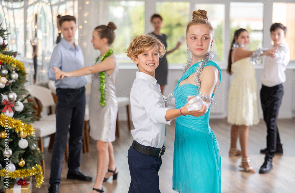 Positive teenage students in festive attire rehearsing ballroom dance number for upcoming Christmas party at college with interested female teacher in background.. Positive teenage students in festive attire rehearsing ballroom dance number for upcoming Christmas party at college with interested female teacher in background..