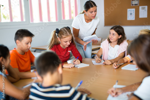 Teacher, together with group of schoolchildren, are looking for solution to complex tasck at round table in a school classroom