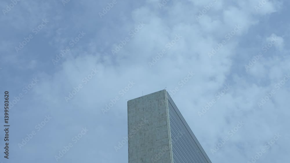 A minimalist upward angle of the United Nations Secretariat Building in NYC against a pale blue sky with light clouds. A minimalist upward angle of the United Nations Secretariat Building in NYC against a pale blue sky with light clouds.