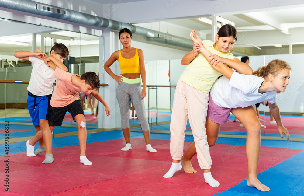 Obraz premium Group of kids exercising self-protection moves on group training. Trainer standing beside and watching them.
