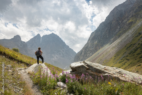 Solo female traveler standing on the rock admiring the mountain view in the scenic valley of Ala Archa National Park in Kyrgyzstan