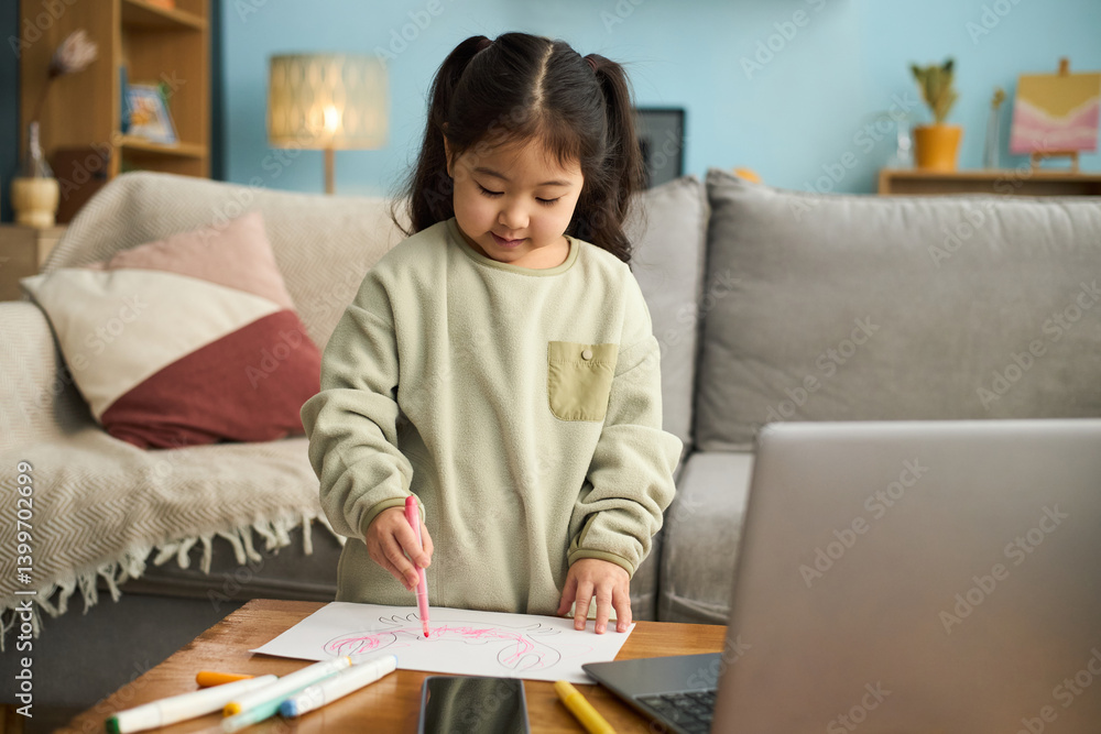 Asian girl sitting in living room drawing with pink marker while laptop rests on table, cozy couch with pillows and lit lamp in background Asian girl sitting in living room drawing with pink marker while laptop rests on table, cozy couch with pillows and lit lamp in background