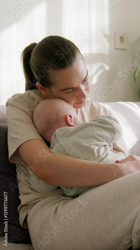 Young happy mother holds baby in her arms to chest in an oasis of peace and love. Loving mother gently lulls her child to sleep in arms by stroking him. Morning sunlight. Happy motherhood