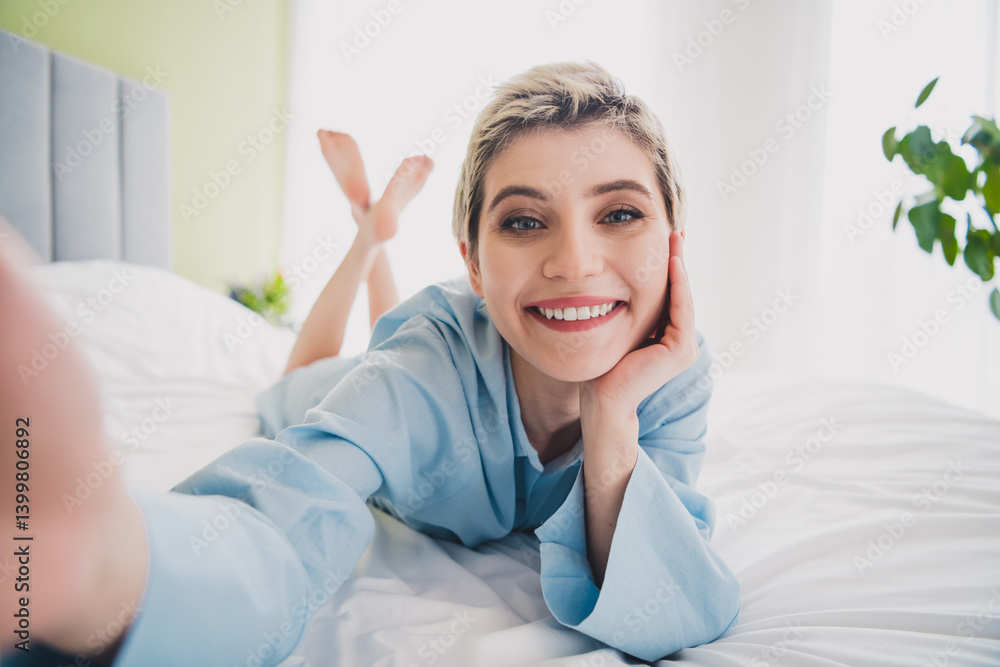Young woman in comfortable blue pajamas smiling joyfully while resting on a bed in a bright and cozy bedroom interior Young woman in comfortable blue pajamas smiling joyfully while resting on a bed in a bright and cozy bedroom interior