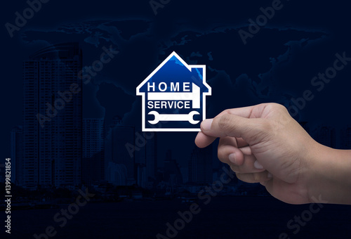Fototapeta Naklejka Na Ścianę i Meble -  Hand holding hammer and wrench with house flat icon in fingers over world map, modern city tower and skyscraper, Business home service concept, Elements of this image furnished by NASA