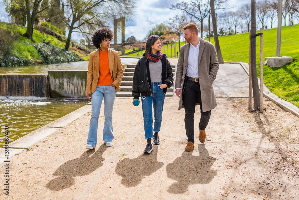 Three colleagues walking and talking in a park by a pond