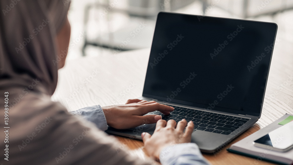 Fototapeta premium Woman in hijab using laptop with blank screen at cafe, back view