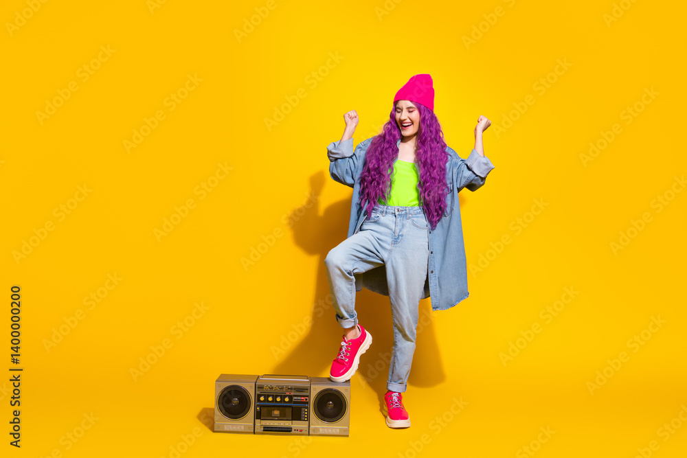 Obraz premium Trendy young woman in vibrant outfit enjoying music with a vintage boombox against a bright yellow background