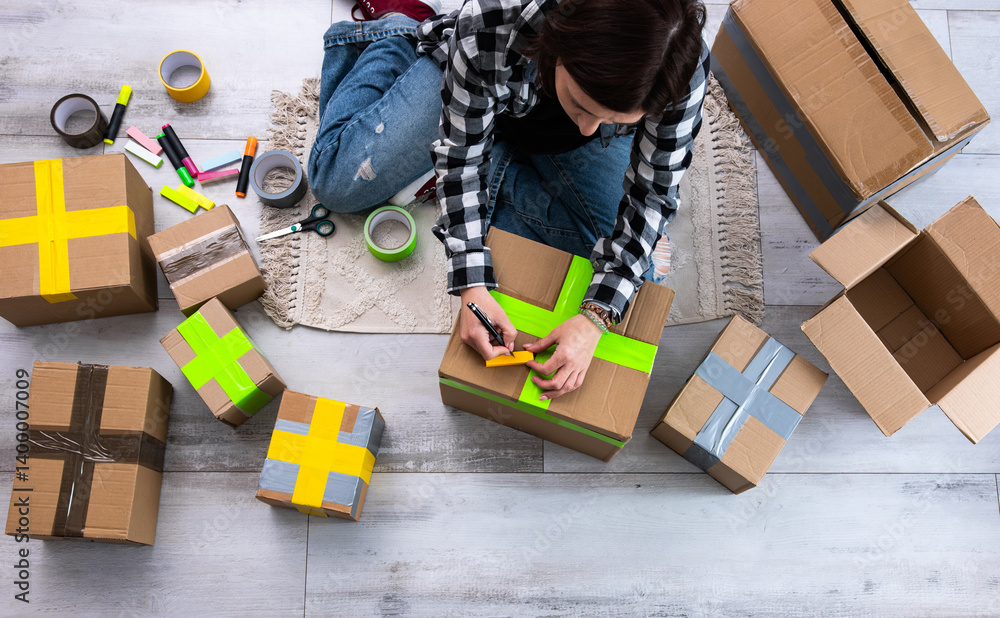 Fototapeta premium Girl Packs Cardboard Boxes And Seals Them With Tape At Home As She Prepares Them For Delivery