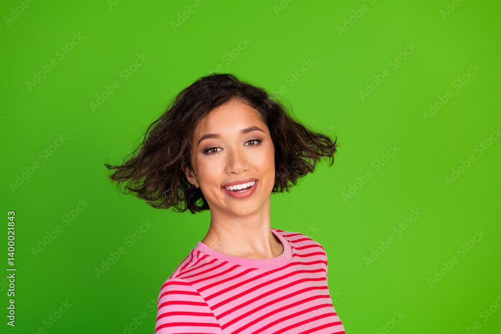 Smiling young woman with short brunette hair in a striped t-shirt standing against a vibrant green background showcasing a lively, cheerful mood Smiling young woman with short brunette hair in a striped t-shirt standing against a vibrant green background showcasing a lively, cheerful mood