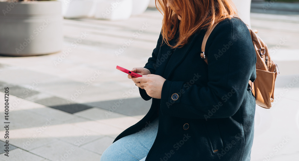Happy woman chatting on phone and relaxing outdoors. Urban, people concept. Smiling 30s redhead woman text messaging on smart phone at sunny day on the city street, spring time
