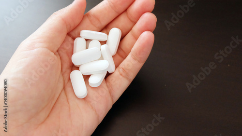 Hand holding a pile of white supplement tablet. With copy space on the right.