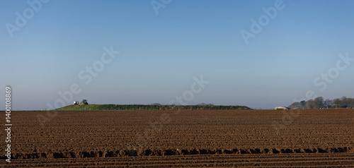 A Tractor and Trailer seen on top of a fenced off Embankment at Hatton Farm near to East Haven with a ploughed field in the foreground.