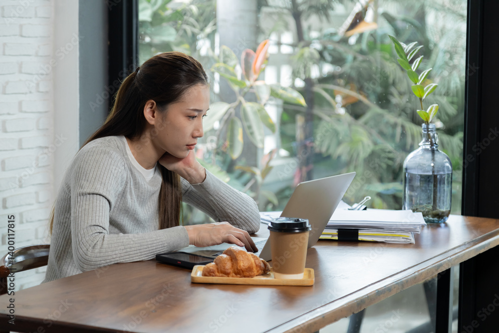 Beautiful Asian woman sitting working anxiously with documents and laptop. Small business owner calculate income and expenses. Attractive businesswoman everywhere working with coffee and croissant. Beautiful Asian woman sitting working anxiously with documents and laptop. Small business owner calculate income and expenses. Attractive businesswoman everywhere working with coffee and croissant.