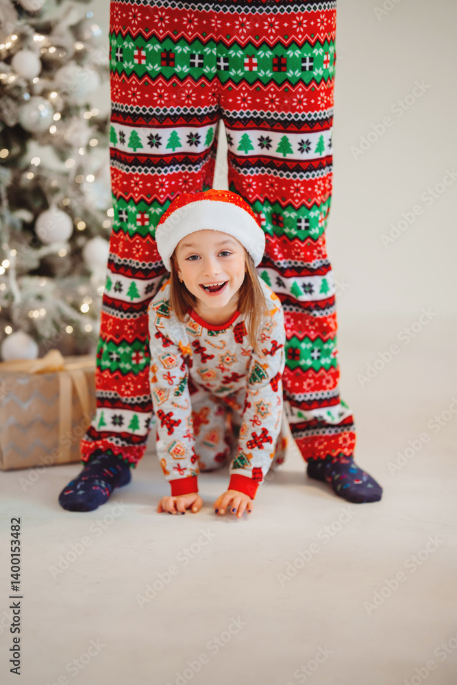 Funny girl in pajamas and hat crawling between daddy's legs. new year holiday