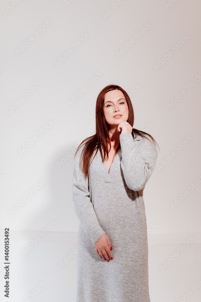 Attractive brunette woman in grey dress against white wall.
