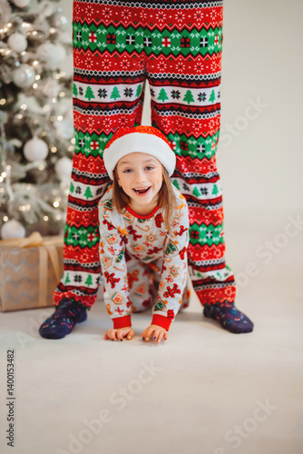 Obraz na płótnie Funny girl in pajamas and hat crawling between daddy's legs. new year holiday w salonie