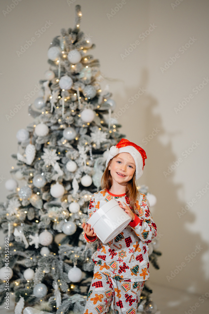 Cute little girl in pajamas with gift in box and christmas tree