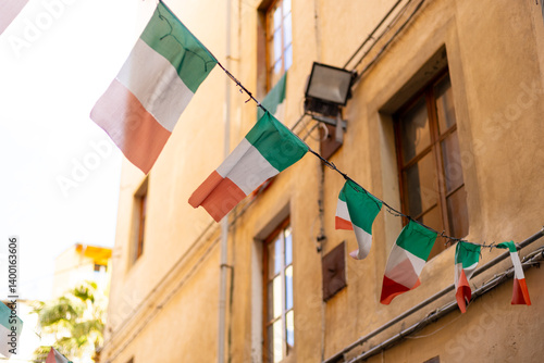 Obraz na płótnie Typical street with houses in Italy. Facade of a yellow building with Italian flags. Italian flag in an old town narrow street of a city in Italy w salonie