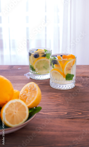 Glass pitcher and cups filled with citrus water, mint, and berries on a rustic wooden table.