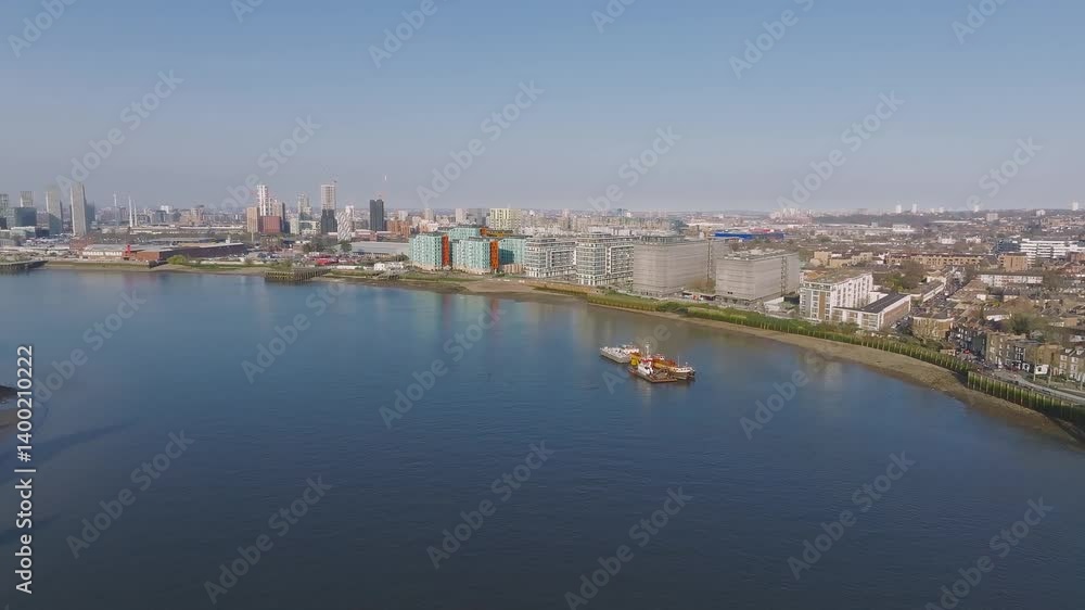 Aerial view of London's riverside with modern buildings, the Thames River, docked vessels, and a skyline of high rise and mid rise structures. Aerial view of London's riverside with modern buildings, the Thames River, docked vessels, and a skyline of high rise and mid rise structures.