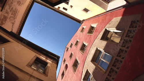 Tiny square or public patio on the street next to the famous old town hall in Regensburg, Germany. Slow motion panning video of looking up between colourful houses or buildings with clear blue sky.