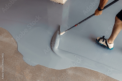 Construction worker applying epoxy resin flooring using a squeegee