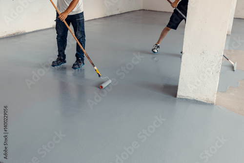 Workers applying epoxy flooring using rollers in a new industrial hall